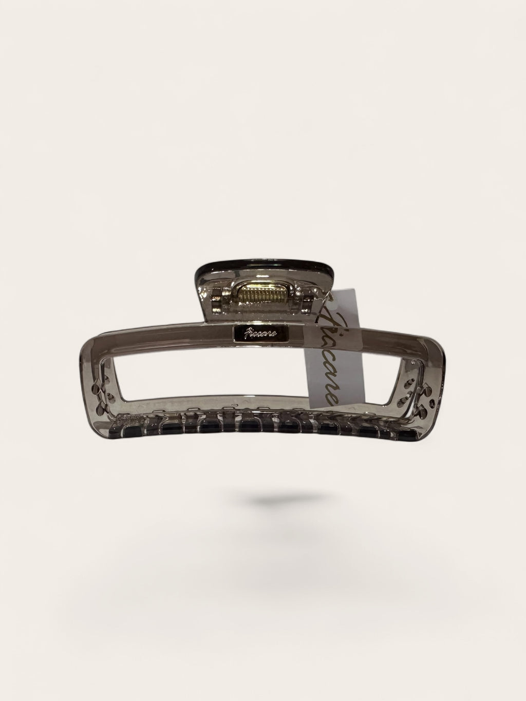 A translucent smoky brown hair claw clip with a textured grip and a small attached paper tag, shown against a solid off-white background.