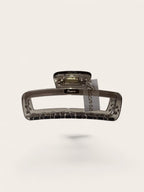 A translucent smoky brown hair claw clip with a textured grip and a small attached paper tag, shown against a solid off-white background.