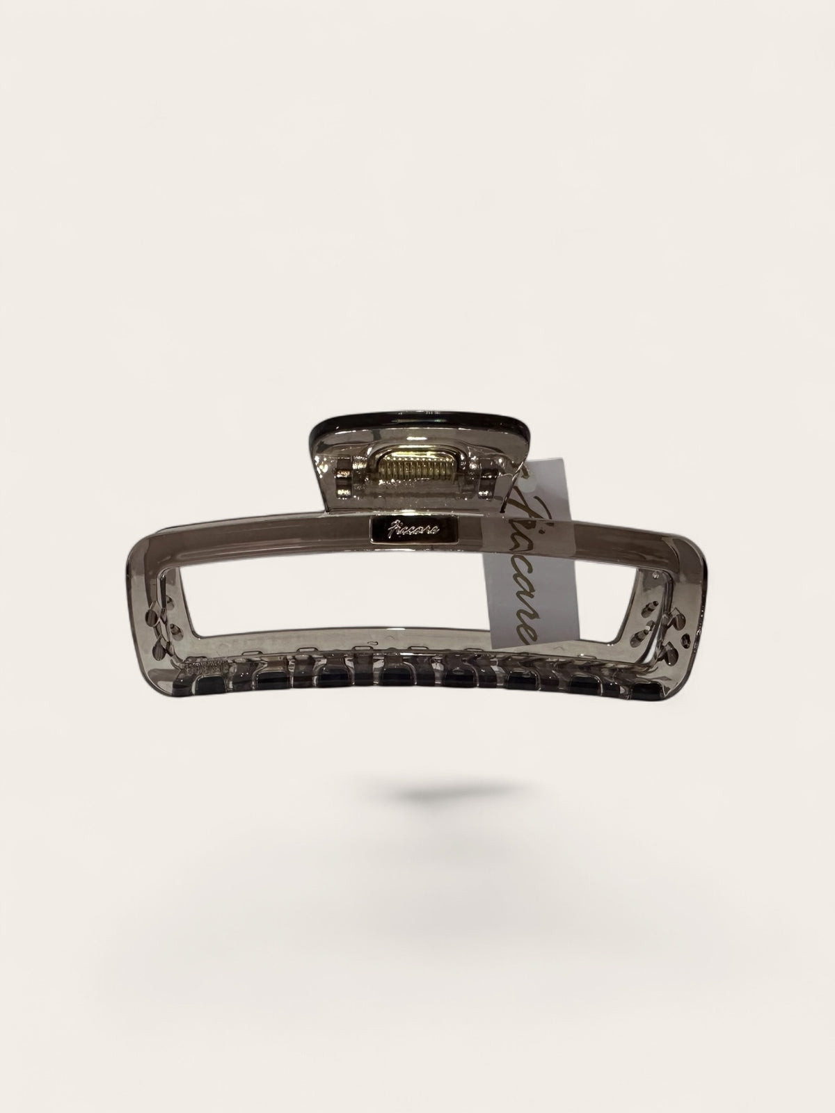 A translucent smoky brown hair claw clip with a textured grip and a small attached paper tag, shown against a solid off-white background.