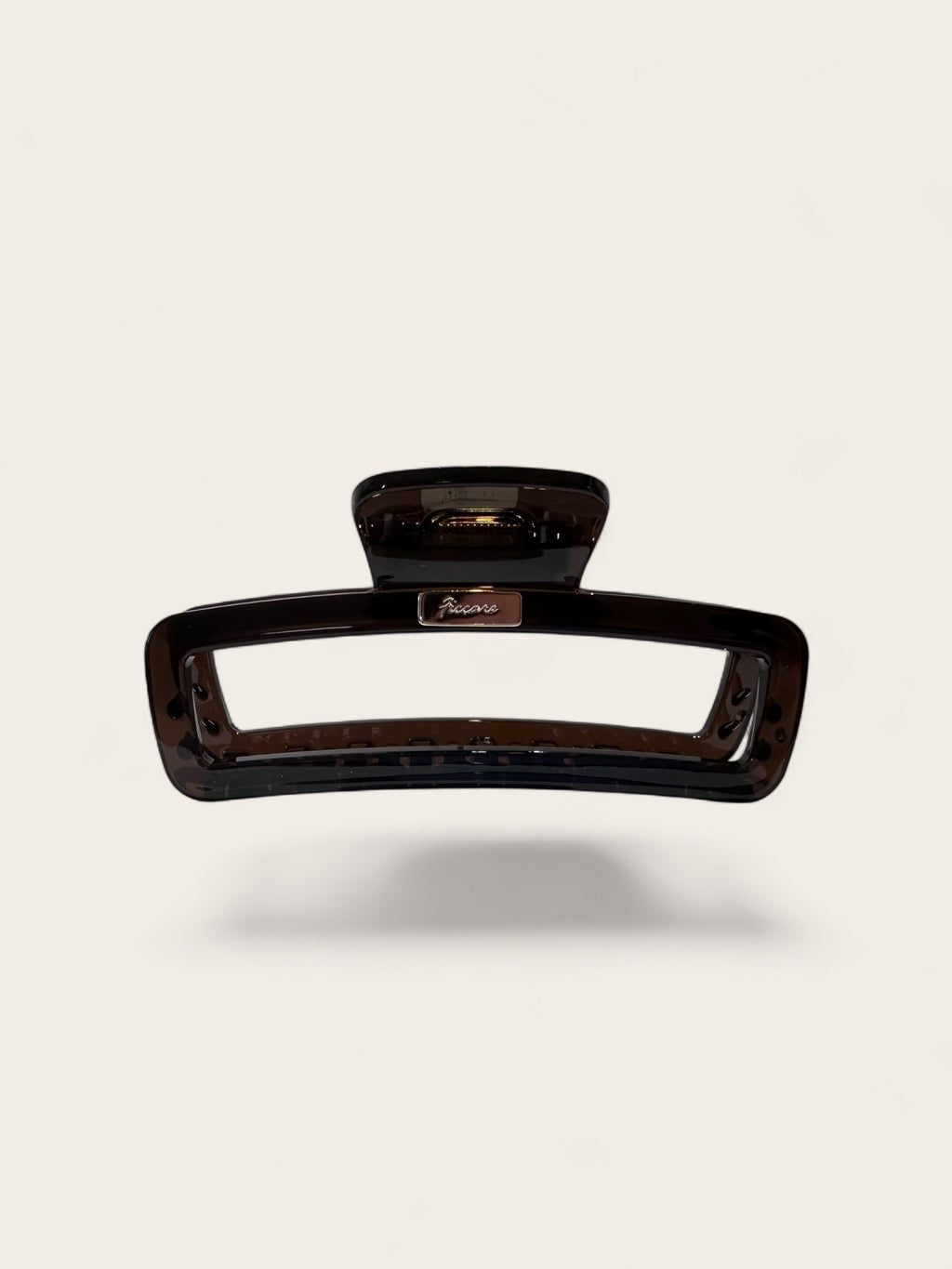 A rectangular hair claw clip in a glossy dark brown tortoiseshell pattern, shown floating against a light beige background with a soft drop shadow.
