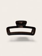A rectangular hair claw clip in a glossy dark brown tortoiseshell pattern, shown floating against a light beige background with a soft drop shadow.