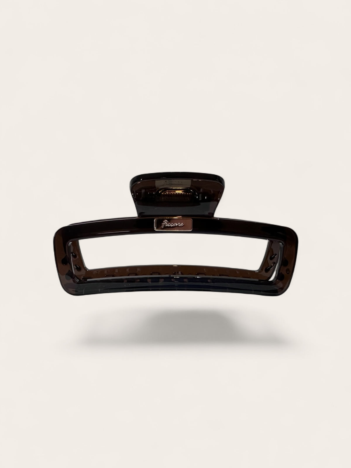 A rectangular hair claw clip in a glossy dark brown tortoiseshell pattern, shown floating against a light beige background with a soft drop shadow.