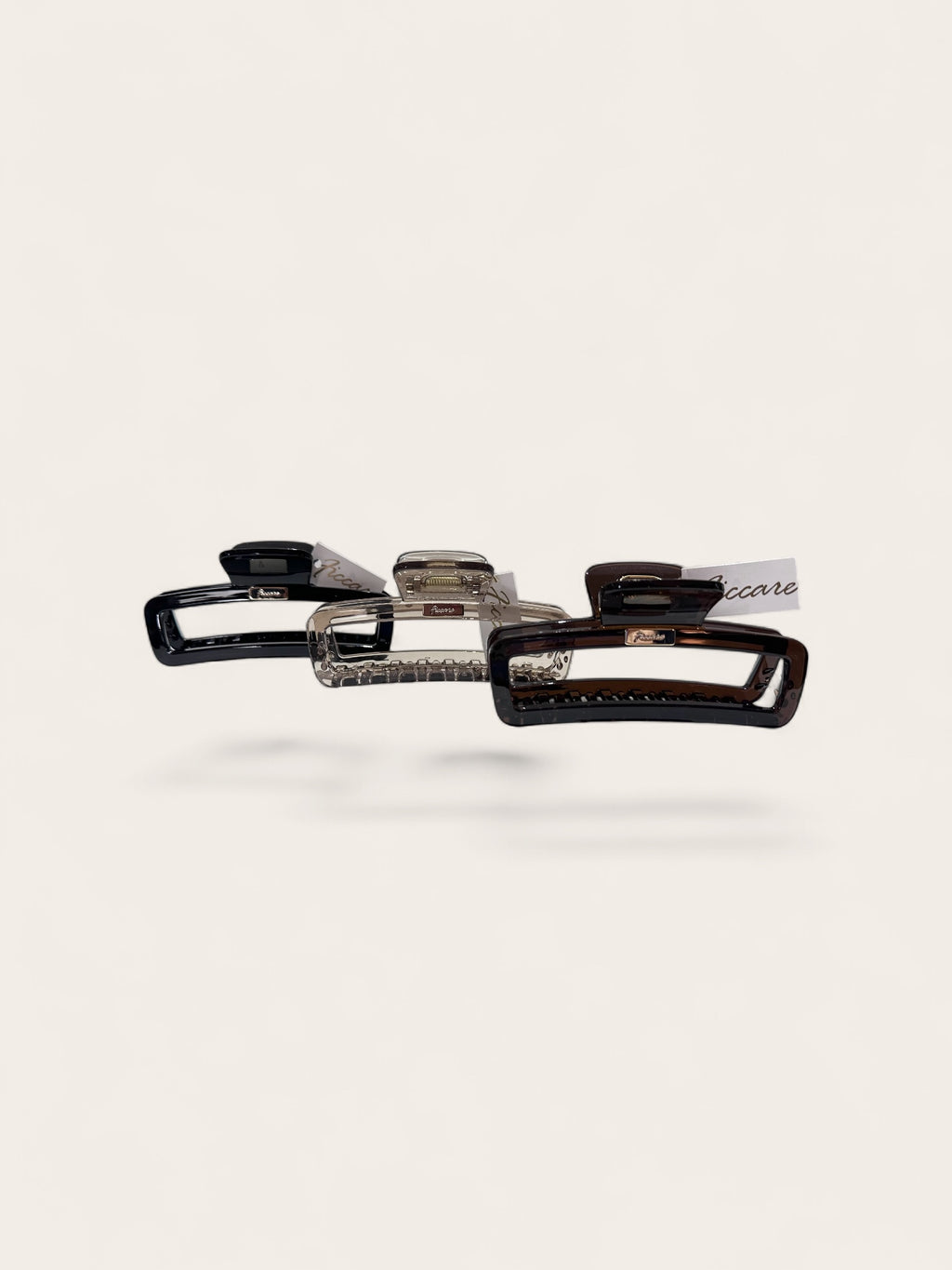 Three hair claw clips in black, clear, and tortoiseshell patterns, arranged horizontally on a light beige background.