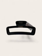 A glossy black hair claw clip with a small gold-tone brand plaque reading 'Ficcare' and a gray paper tag attached, shown on a clean off-white background.