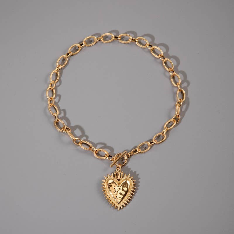 Gold chain bracelet with a heart-shaped pendant on a gray background